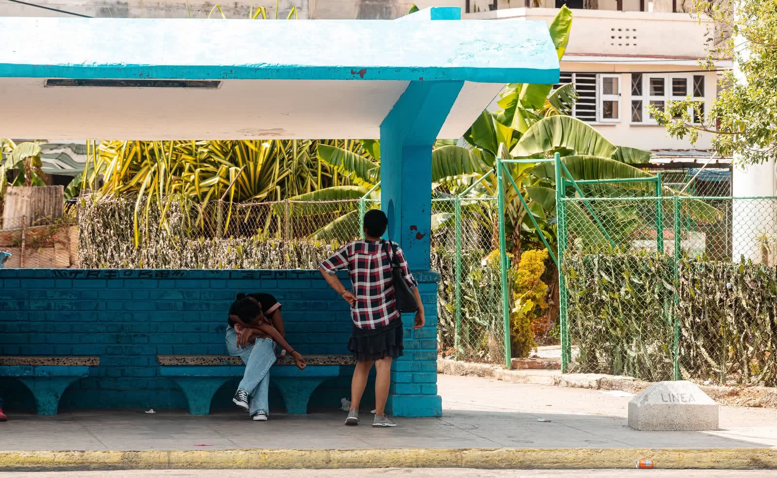 Una parada de guagua azul en Cuba, con gente esperando a la sombra